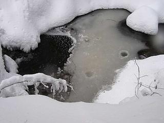 Wide shot of semi-frozen creek with snow "plumpfs"