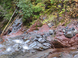 At the crossing of Kulshan Creek about 1.5 miles in, the first volcanic rocks along the trail are in the creek at the ford.  The creek flows over a very young, post- Pleistocene glacial Mount Baker lava, the andesite of Glacier Creek that erupted from Carmelo Crater at Mount Baker's summit.. It is best exposed just below the crossing. This is the youngest lava from the Mount Baker cone reached by any trail. The rock is a scrap of an intracanyon lava flow, which entered and flowed down Glacier Creek at least as low as 2000 feet  at The Palisades (shown on the Groat Mountain 7.5-minute topo map). Here, a branch of the flow extended down the steep drainage of Kulshan Creek.Volcanologist Wes Hildreth estimates that 90% of the intracanyon lava has been eroded. The remainder of the flow at the Palisades is 180 feet thick  and beautifully columnar- bushwhacking and fording is required to reach it, but it is a worthwhile cross country geology adventure. The lava probably once extended much farther down Glacier Creek, perhaps as far as the Nooksack valley, 3 miles  below the lowest remnant. The canyon-filling portion of the flow low down in Glacier Creek has not been glaciated. Most of the fractured lava was removed by Glacier Creek as it re-established itself after the valley was plugged by the thick lava. A K-Ar determination from the lava in Kulshan Creek below the trail crossing gave an age of 14  9 thousand years. The imprecision is unfortunate, but is due to the scarcity of 40 Ar in the sample; this is itself an indication of relative youthfulness . The composition of this lava is identical with the highest and therefore youngest lava at the top of the Roman Wall just below the summit of Mount Baker, strong evidence that this andesite is one of the last lavas erupted from the volcano.