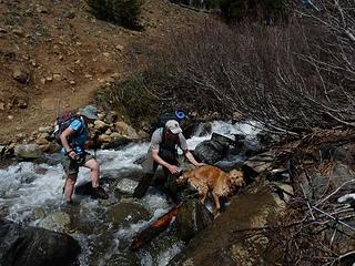 Gus' friends assist him across the rapidly flowing creek