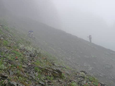 This descent would present a number of challenges. The first of which was some steep, hard scree near the top of a potentially long slide to an uncertain landing. We crossed it carefully in the wet conditions (photo: Jeff).
